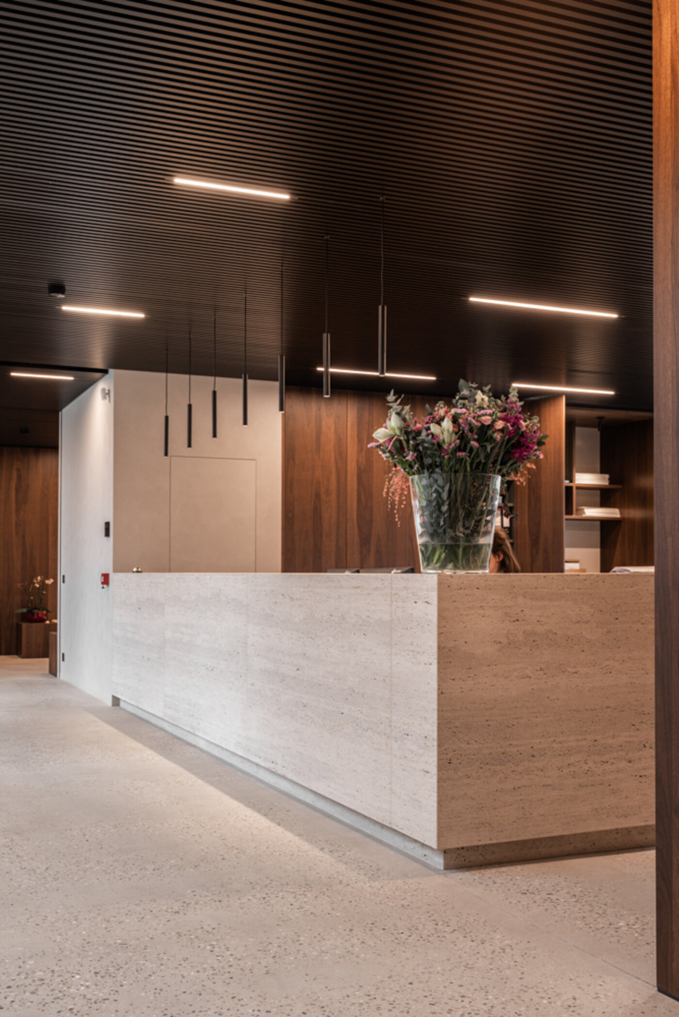 Straatzicht van het notariaat in Meulebeke, ontworpen door GC Architecten: een licht gekleurd volume met verticale gevellamellen, donkere raamkaders en een lagere zijvleugel, omgeven door een strakke haag en siergrassen.