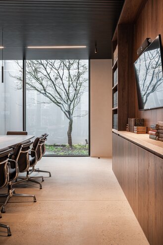 Straatzicht van het notariaat in Meulebeke, ontworpen door GC Architecten: een licht gekleurd volume met verticale gevellamellen, donkere raamkaders en een lagere zijvleugel, omgeven door een strakke haag en siergrassen.