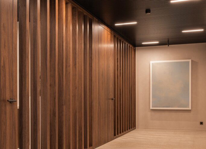 Straatzicht van het notariaat in Meulebeke, ontworpen door GC Architecten: een licht gekleurd volume met verticale gevellamellen, donkere raamkaders en een lagere zijvleugel, omgeven door een strakke haag en siergrassen.