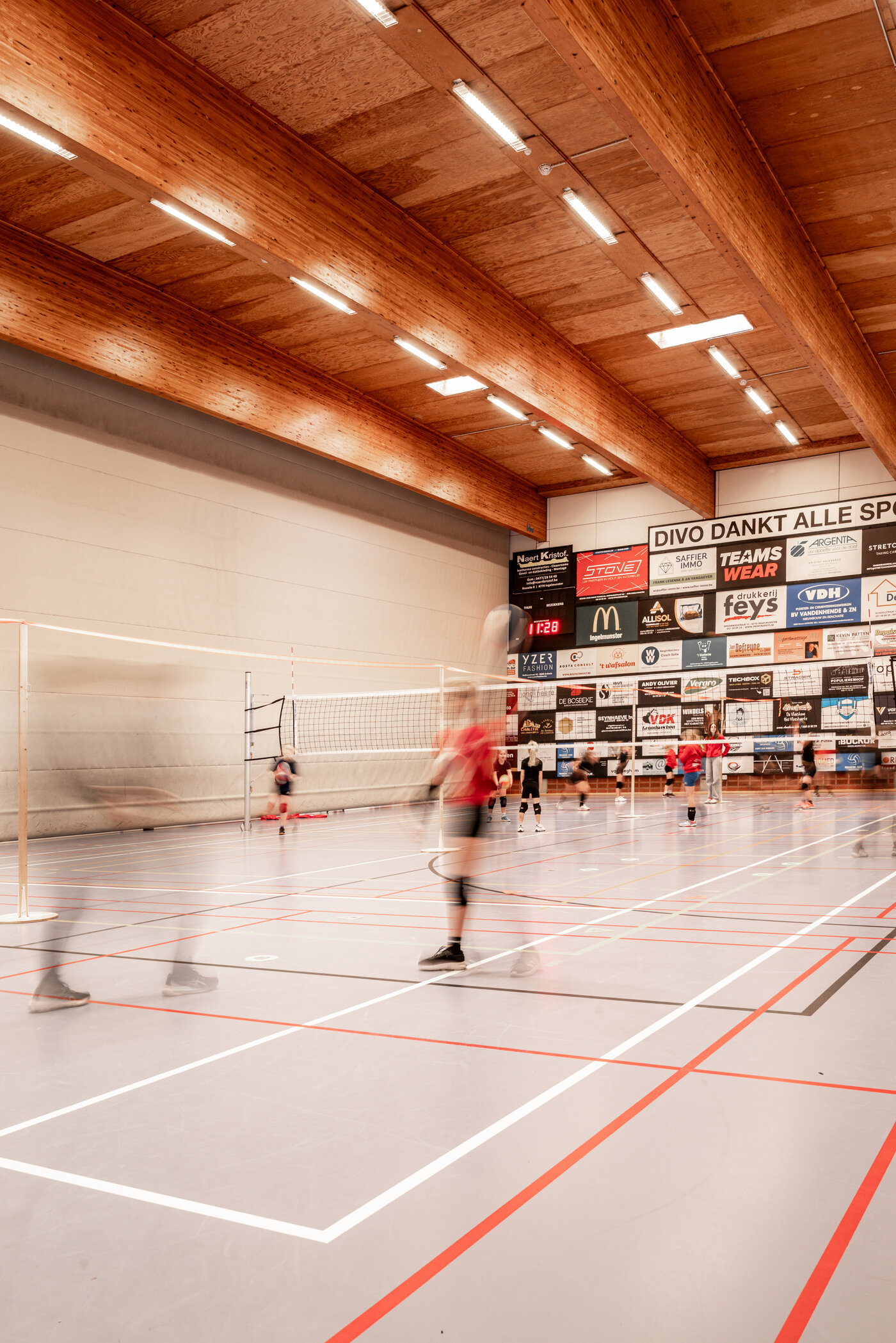 Zicht op sporthal met houten liggers, volleybal training bezig