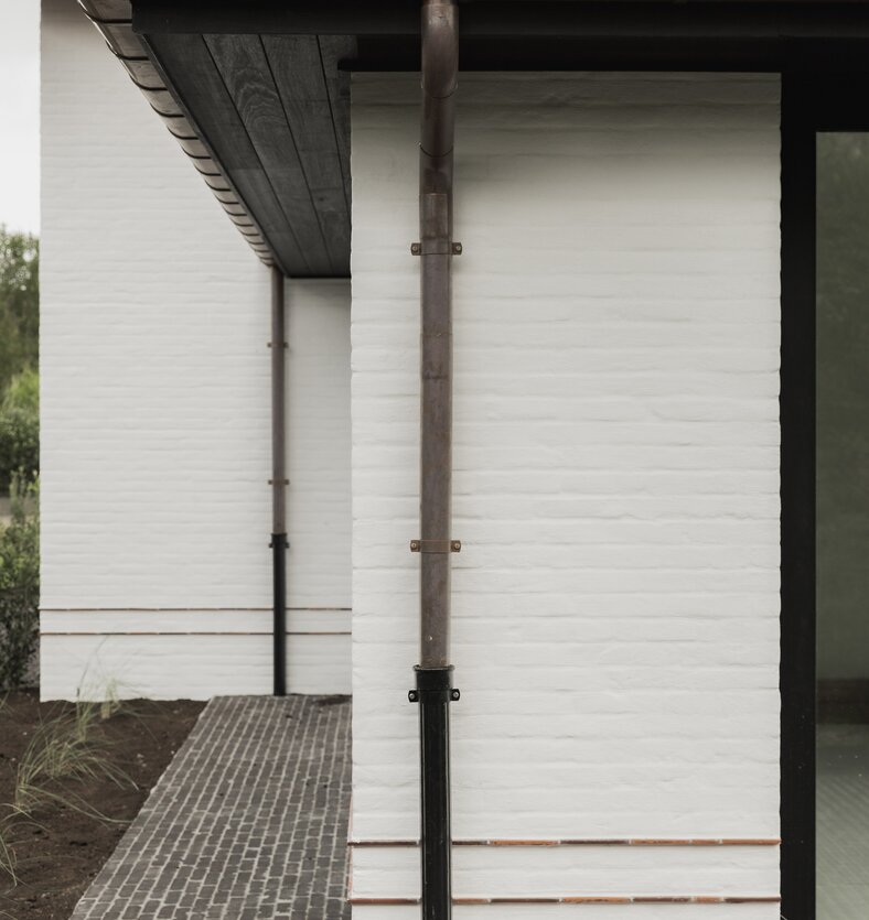 zicht op hoek van hedendaagse cottagevilla in Knokke door GC architecten. Witgeschilderde bakstenen onder rode pannendaken. Koperen afvoeren.  | © Bert Demasure