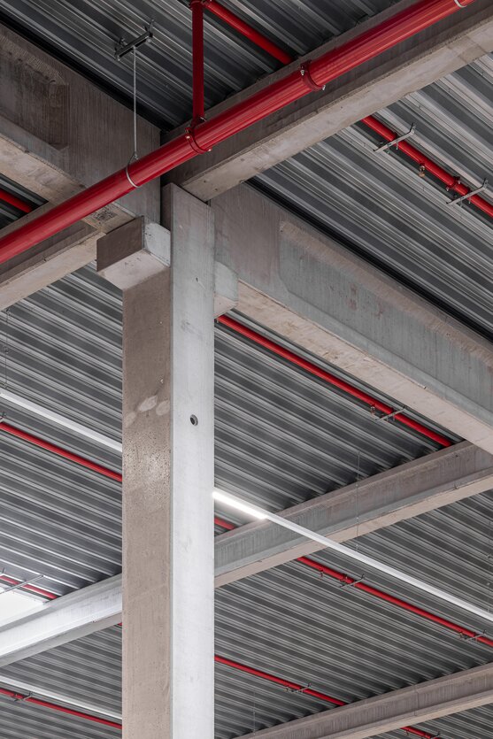 Detail van de betonstructuur met kolommen, liggers en staalplaatdak met technische leidingen in een industrieel gebouw | © Michiel Vergauwe