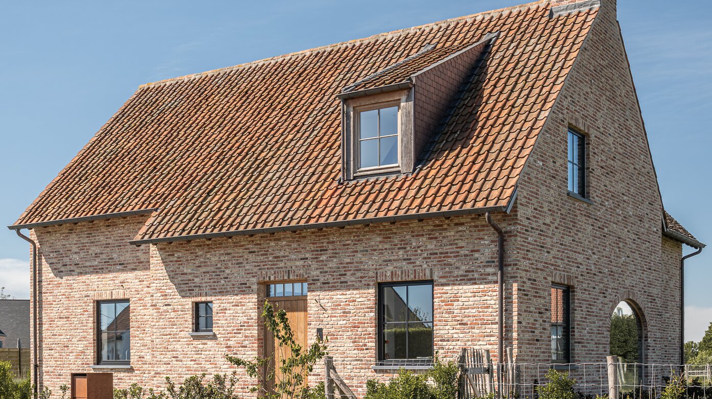 Voorgevel van een landelijke woning met bakstenen muren, houten voordeur en zadeldak