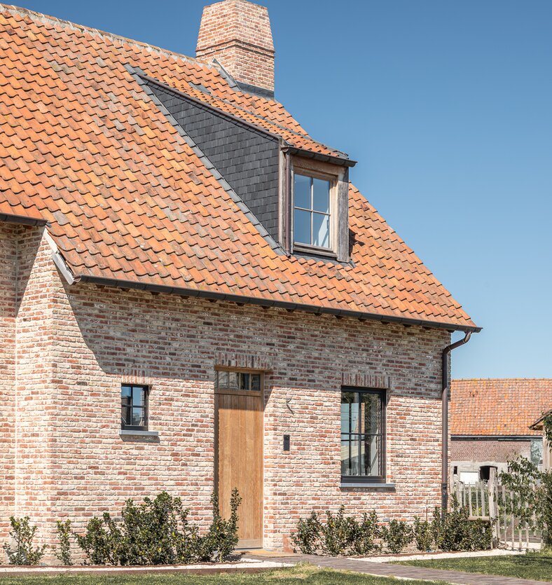 Voordeur en dakkapel in traditionele bakstenen woning met terracotta dakpannen en schoorsteen