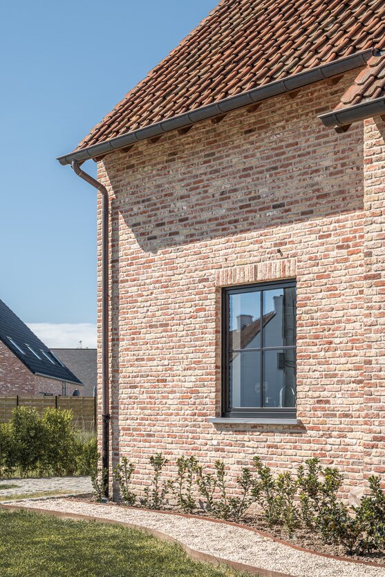 Detail van bakstenen gevel met zwart kozijn en rood pannendak