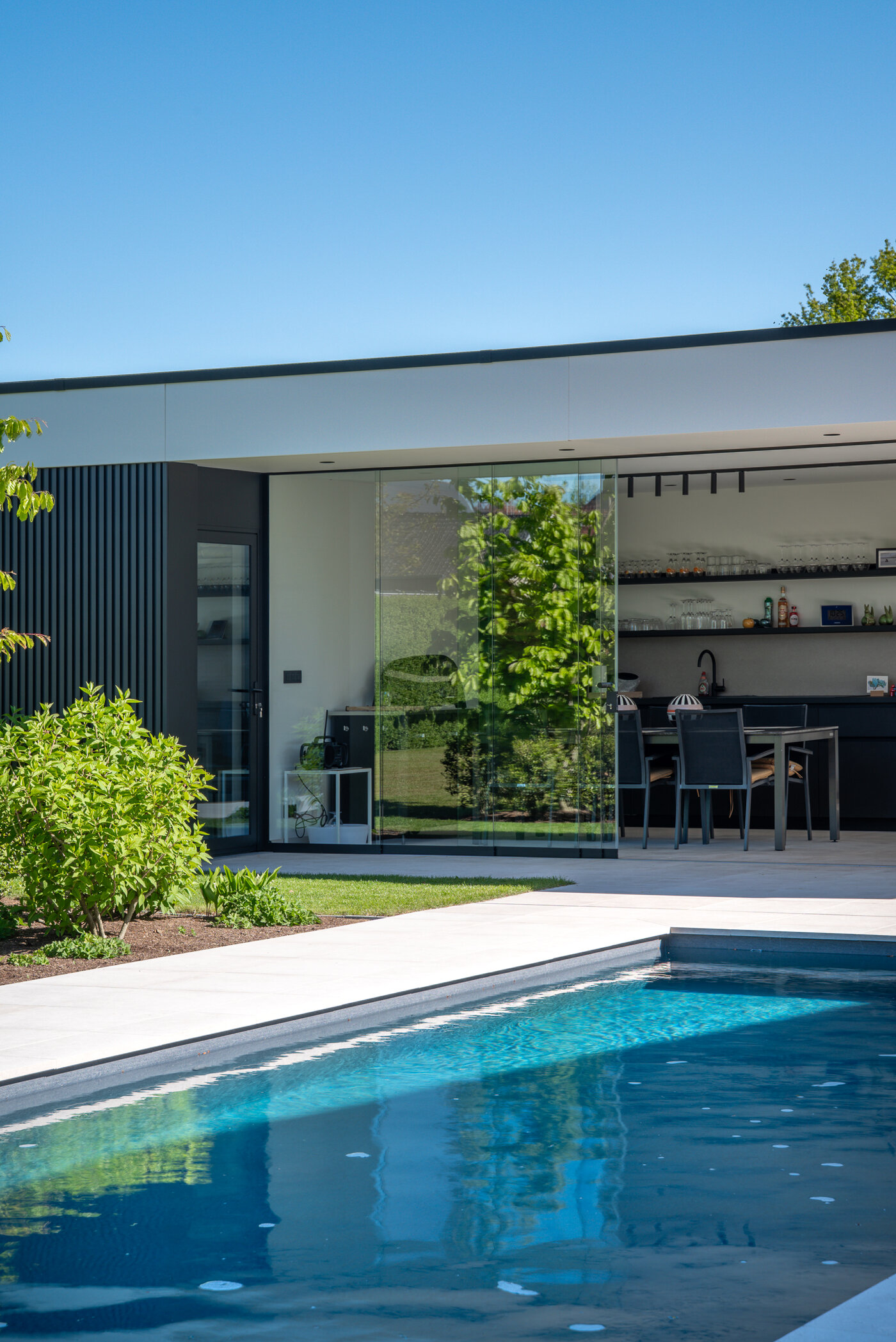 Open poolhouse van GC Architecten met glazen schuifdeur en eetruimte naast het zwembad