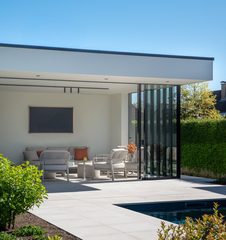 Overdekte zithoek met openschuivende glazen wand naast een zwembad in poolhouse van GC Architecten