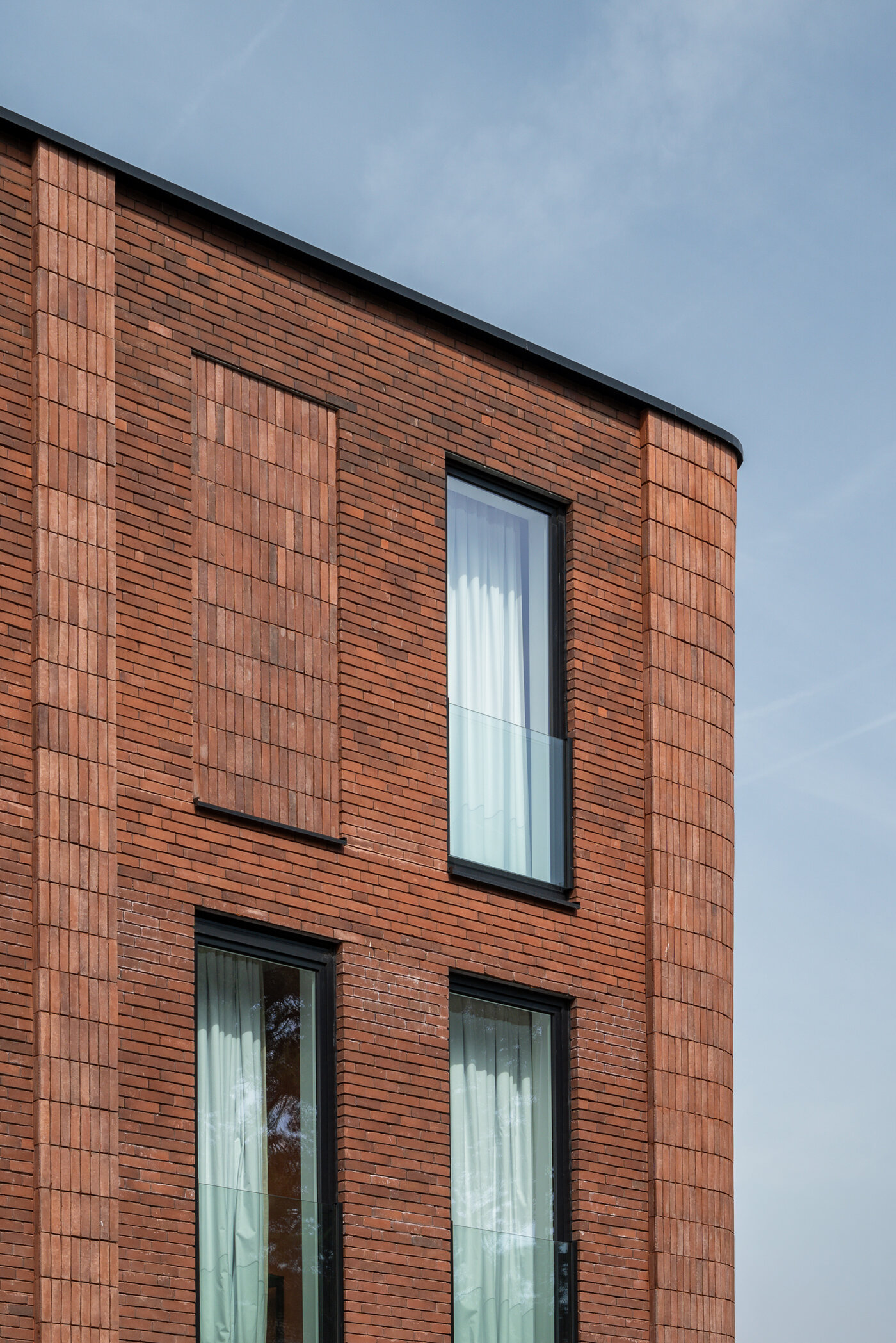 Detail van roodbruine bakstenen gevel met afgeronde hoek en verticale raamopeningen