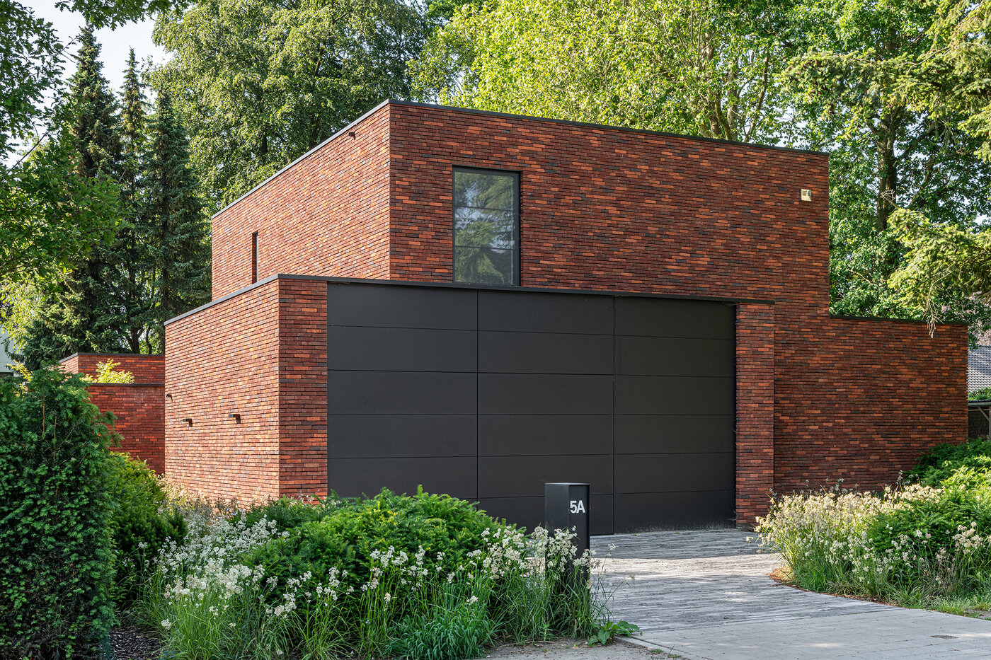 Zijaanzicht van een bakstenen woning met verspringende volumes en een grote zwarte garagepoort, ontworpen door GC architecten.